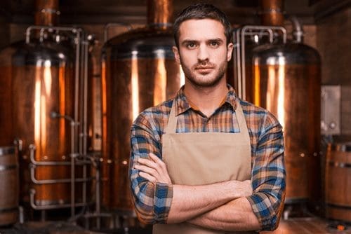 Distiller in front of tanks at a distillery